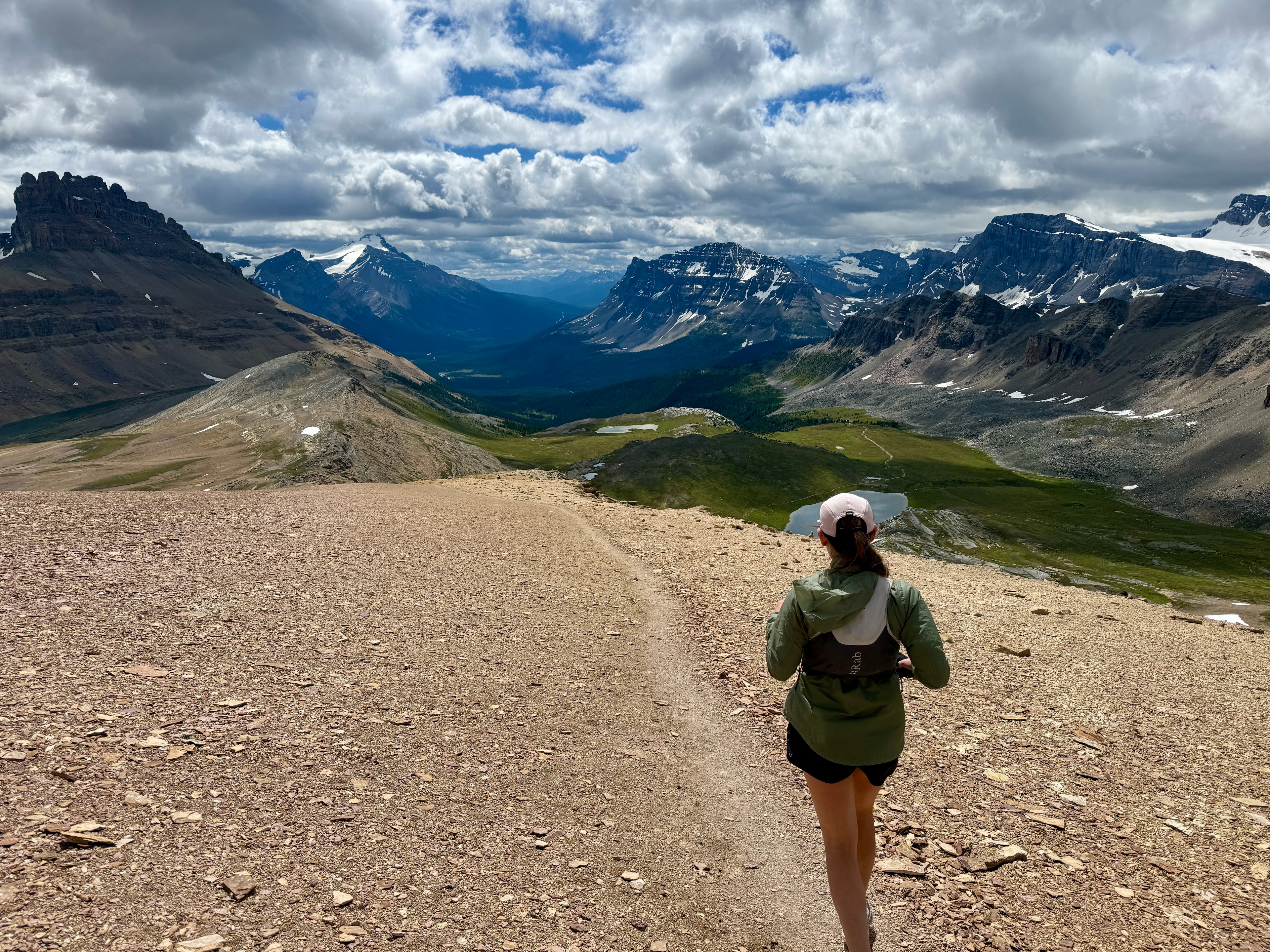 Runner descending a rocky alpine trail with sweeping mountain valley views